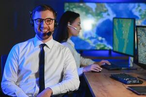 In Monitoring Room Technical Support Specialist Speaks into Headset. His Colleagues are Working in the Background photo