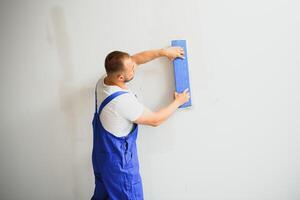 Portrait of a worker in overalls and holding a putty knife in his hands against the plastered wall background. Repair work and construction concept photo