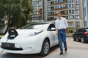 portrait of young handsome man in casual wear, standing at the charging station. Eco electric car concept photo