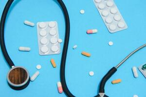 Scattered white pills on blue table.Medical, pharmacy and healthcare concept. Blue background white pills with a medical statoscope, top view photo