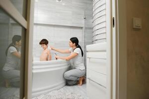 Mother washing little son in bathroom photo