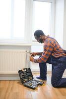 Man in workwear overalls using tools while installing or repairing heating radiator in room photo