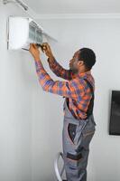 African American electrician repairing air conditioner indoors photo