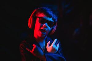 teen boy listening to music with headphones, neon light trending portrait. Looks at the camera photo