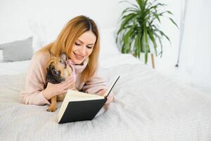 Girl reading a book. Cute girl reading a book with her dog at home. Pretty stylish girl. photo