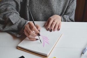 Woman paints in a sketchbook. Tools for painting on the white wooden desk. Painter work. photo