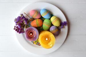 Colorful easter eggs with flowers and candles in the plate. Beautiful easter background. Easter card. Homemade holiday decor. photo