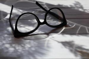 Spectacles in black frame on white wooden table in sunshine. photo