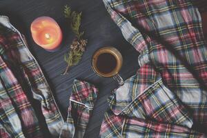 A cup of coffee, pajamas and lighted candle on the wooden background. Cozy home style. Atmospheric picture. photo