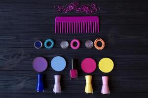 Colorful and bright cosmetics. Beauty care tools. Beauty salon. Girl's paradise. Nail polishes, sequins, pink hair bands and comb on a dark blue wooden desk. Bright still life of beauty instruments. photo