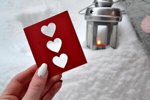 Red love card in female hand. Candle lantern on the snowdrift. Cold season. Hygge style. photo