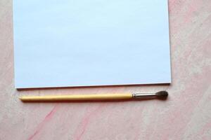 The sheet of white paper and brush on the textured desk. Top view. Tools for painting. photo