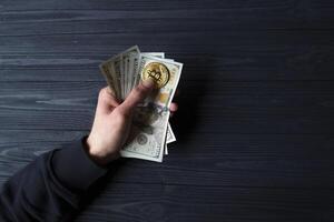 Golden bitcoin and dollars in male hand on a dark blue wooden background. Gold coin of cryptocurrency. photo