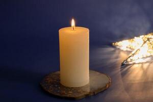 Burning candle and Christmas lights on dark blue background. photo