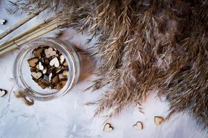 Wooden hearts in a jar and bulrush plant on a grey textured background. Stylish still life. photo