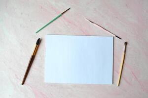 The sheet of white paper and brushes on the textured desk. Top view. Tools for painting. photo