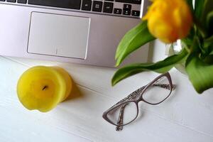 Laptop, flowers, eyewear on a white desk. Beautiful workplace top view. Office workplace. photo