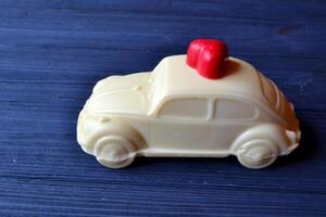 White chocolate in a form of car with red candy in a form of heart on the dark blue wooden table. photo