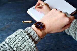 negocio mujer mirando a el reloj en su mano y escritura en el cuaderno. elegante negocio antecedentes. foto