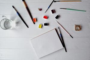 Tools for painting on the white wooden desk. Brushes, paper and paints on the table. Painter's workplace. photo