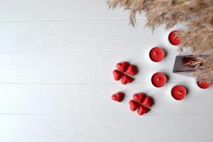 Red candies in a form of heart and red candles on the white wooden table. Background for greeting card on Valentine's day with place for text. photo