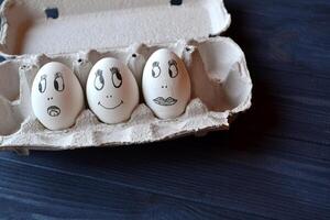 Eggs with a faces in a container box on the wooden table. Creative easter background. Happy easter day. photo