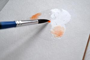 Woman paints in a sketchbook. Tools for painting on the white wooden desk. Painter work. photo