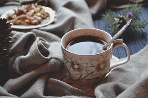 A cup of coffee, nuts in the plate, branch of spruce, knitted sweater in cozy atmosphere on the dark blue wooden background. Atmospheric flat lay in hygge style. photo
