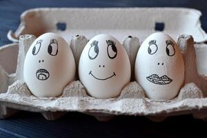 Eggs with a faces in a container box on the wooden table. Creative easter background. Happy easter day. photo