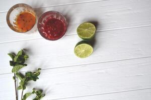 Ingredients for cooking natural tea. Mint, lime, raspberry and sea buckthorn jams on the white wooden table. photo