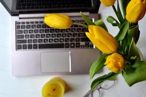 Laptop, flowers, eyewear on a white desk. Beautiful workplace top view. Office workplace. photo