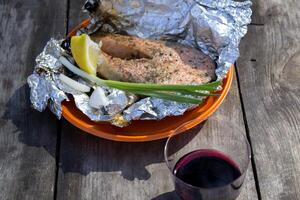 A trout cooked at the stake in orange plate on a wooden table outdoor. photo