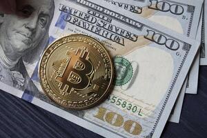 Golden bitcoin and dollars in male hand on a dark blue wooden background. Gold coin of cryptocurrency. photo