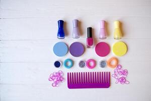 Colorful and bright cosmetics. Beauty care tools. Beauty salon. Girl's paradise. Nail polishes, sequins, pink hair bands and comb on the white wooden desk. Bright still life of beauty instruments. photo