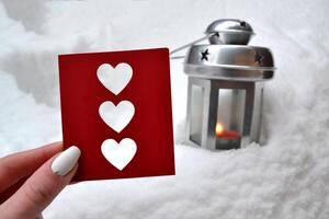 Red love card in female hand. Candle lantern on the snowdrift. Cold season. Hygge style. photo