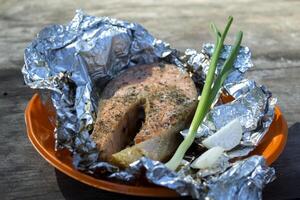 A trout cooked at the stake in orange plate on a wooden table outdoor. photo