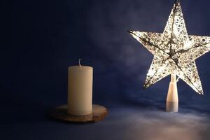 Light star and candle on dark blue background. photo