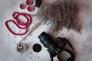 Camera, red beads, wooden hearts and bulrush plant on a grey textured background. Stylish still life. photo