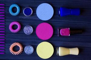 Colorful and bright cosmetics. Beauty care tools. Beauty salon. Girl's paradise. Nail polishes, sequins, pink hair bands and comb on a dark blue wooden desk. Bright still life of beauty instruments. photo