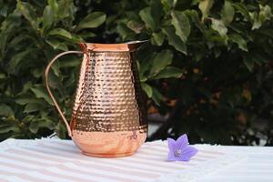 Copper jug and flower on the table, outdoor. Still life with pitcher and flower. photo