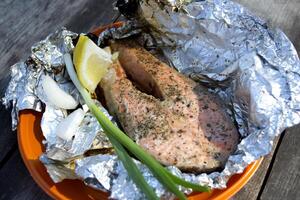 A trout cooked at the stake in orange plate on a wooden table outdoor. photo