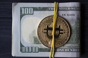 Golden bitcoin and dollars in male hand on a dark blue wooden background. Gold coin of cryptocurrency. photo