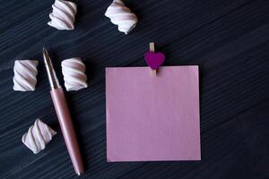 The sheet of pink paper, pen and marshmallow on a dark blue wooden table. photo