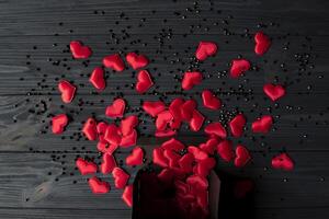rojo corazones son vertido fuera de un negro regalo caja en un oscuro azul de madera mesa. foto