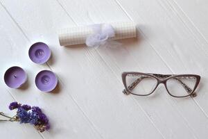 Letter, glasses, candle and flower on the white table. Beutiful female objects on the white wooden background. Flat lay in violet color. photo