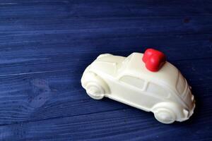 White chocolate in a form of car with red candy in a form of heart on the dark blue wooden table. photo