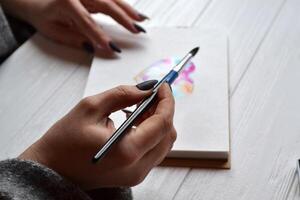 Woman paints in a sketchbook. Tools for painting on the white wooden desk. Painter work. photo