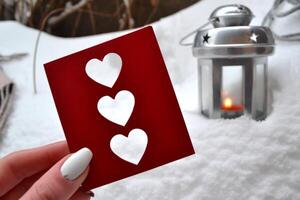 Red love card in female hand. Candle lantern on the snowdrift. Cold season. Hygge style. photo