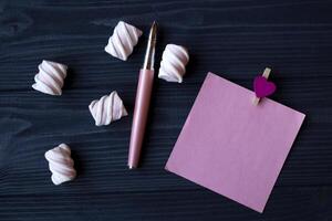 The sheet of pink paper, pen and marshmallow on a dark blue wooden table. photo