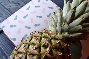 Pineapple and notebook on the dark blue wooden table. Abstract stylish background. photo